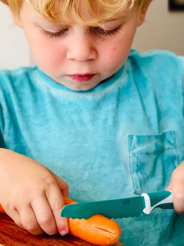 a child using a blue kiddikutter kid safe knife to cut a carrot