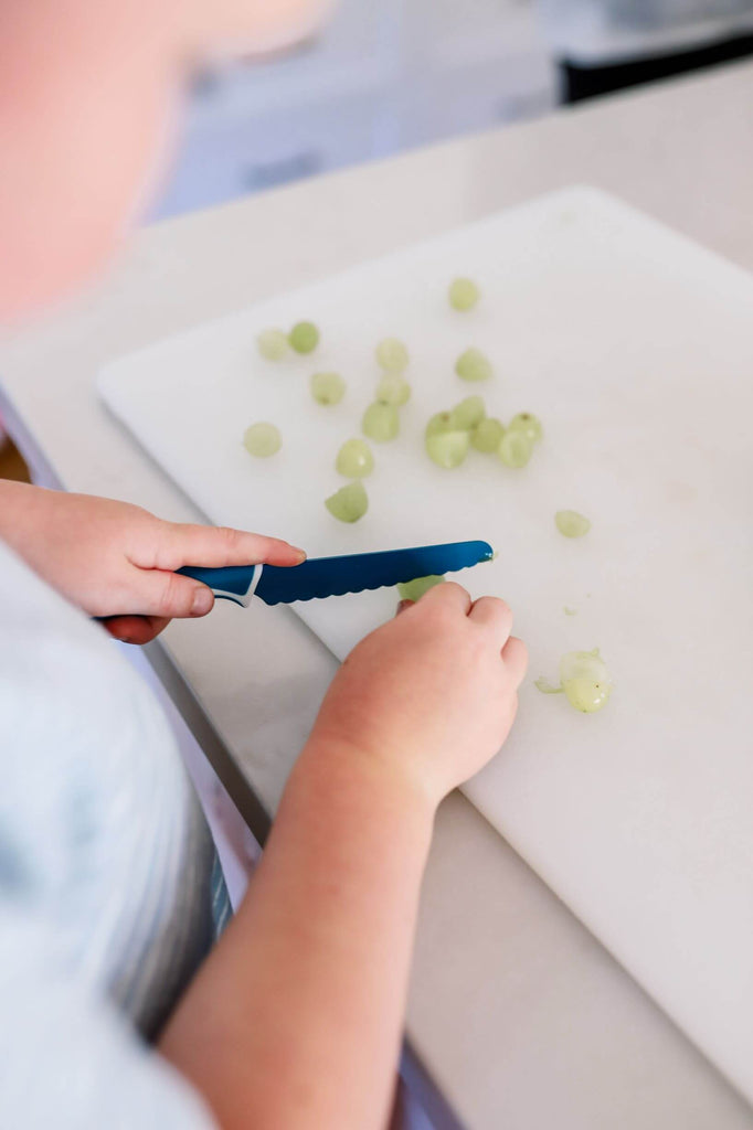 A child using a kiddikutter kid safe knife to cut grapes #color_Kiddikutter-Child-Safe-Knife-Blue