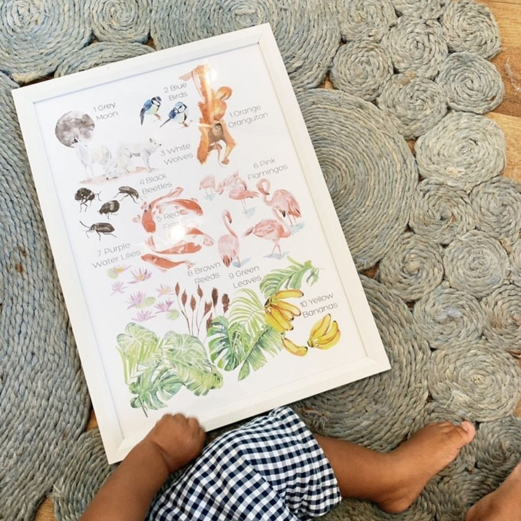 Baby sitting with a white framed print of numbers and colours with hand-illustrated watercolor at